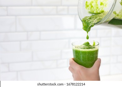 Woman pours green smoothie from a blender into a glass. Girl makes a healthy smoothie from a green apple and spinach. Morning detox for a healthy lifestyle, weight loss, ketone diet, raw food diet - Powered by Shutterstock