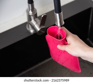 A Woman Pours Hot Water Into A Medical Heating Pad From The Tap. Treatment Of Diseases With Heat