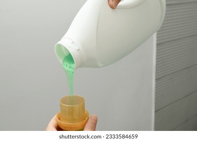 Woman pours liquid washing gel into plastic cap. Concept of washing clothes, domestic routine and household chores. Close up of attractive female pouring liquid green gel into bottle cap. - Shutterstock ID 2333584659