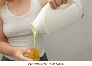 Woman pours liquid washing gel into plastic cap. Concept of washing clothes, domestic routine and household chores. Close up of attractive female pouring liquid green gel into bottle cap. - Shutterstock ID 2334223183
