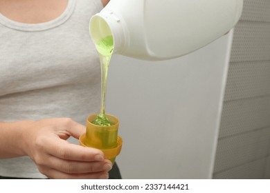 Woman pours liquid washing gel into plastic cap. Concept of washing clothes, domestic routine and household chores. Close up of attractive female pouring liquid green gel into bottle cap. - Shutterstock ID 2337144421