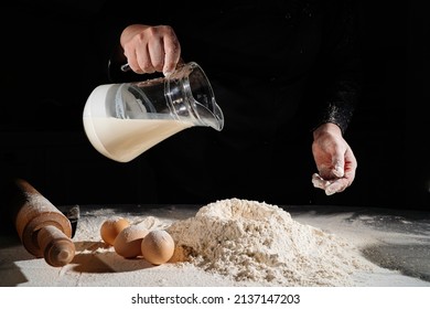 woman pours milk from jug into flour to knead dough on black background. the concept of homemade baking and cooking school. recipes for bread, pizza and pies. family business. professional bakery.