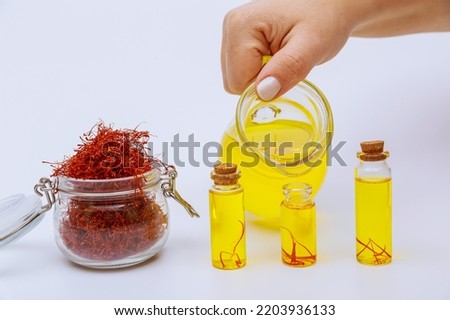 A woman pours a saffron drink into small jars. Saffron tea and a full jar of dry red stamens on a white background.