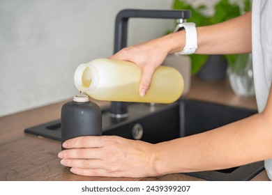 A woman pours soap or detergent from recycled packaging into a reusable bottle in kitchen. Eco-friendly lifestyle concept. High quality photo - Powered by Shutterstock