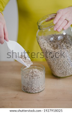 Woman pours sunflower seeds to glass jar