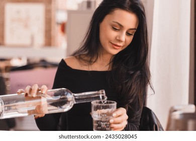 Woman pours water into a glass from a glass bottle. Brunette woman have a good time in cafe, she look happy and smiling. - Powered by Shutterstock