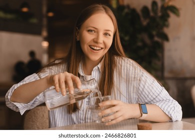 Woman pours water into a glass from a glass bottle. Blonde woman have a good time in cafe, she look happy and smiling. Girl wear stripped shirt. - Powered by Shutterstock