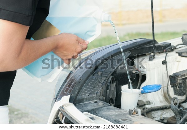 Woman pours windshield cleaning\
fluid. Flow windshield fluid into the windshield washer reservoir.\
Water tank wiper on car engine room, Maintenance\
concept.