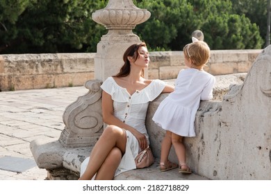 Woman Pouting Lips Near Toddler Daughter On Stone Bench Of Puente Del Mar Bridge In Valencia