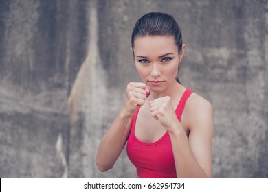 Woman power, self defence concept. Close up portrait of attractive serious fit boxer, ready for fight, on concrete wall background, wearing pink fashionable sport wear