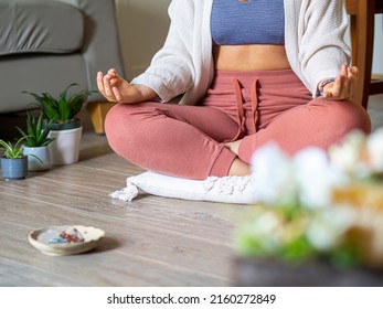 Woman Practice Mediation At Home With Crystals And Plants. Unrecognizable Young Adult Meditating In Quiet And Relaxing Room Sitting In Lotus Position On A Pillow. Mental Health And Stress Relief.