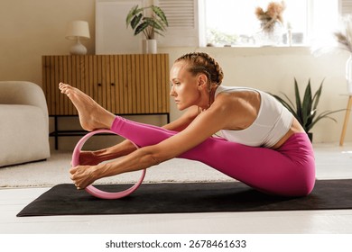 Woman practices a deep hamstring stretch using a yoga wheel to improve flexibility mobility and posture in a calm home studio