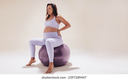 Woman practices prenatal care and self-care during pregnancy. Engaging in fitness exercises, she uses an exercise ball for stability and strength. Pregnant woman focusing on her wellbeing and health. - Powered by Shutterstock