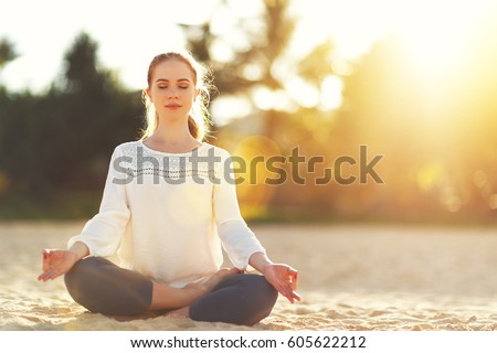 woman practices yoga and meditates in the lotus position on the beach

