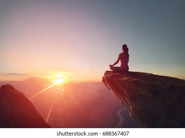 Woman practices yoga and meditates on the mountain.