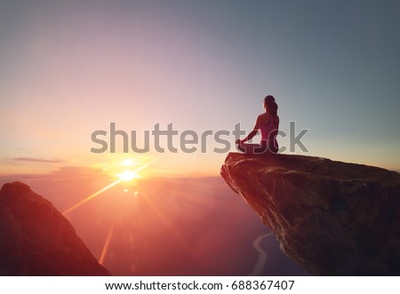 Woman practices yoga and meditates on the mountain.