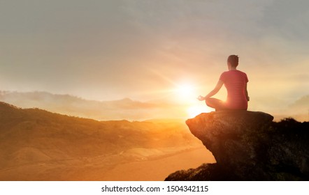 Woman practices yoga and meditating on the mountain sunset background.