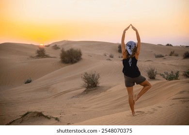 A woman practices yoga in a peaceful desert landscape, silhouetted against a vibrant sunset. The tranquil setting emphasizes relaxation, mindfulness, and connection with nature. - Powered by Shutterstock