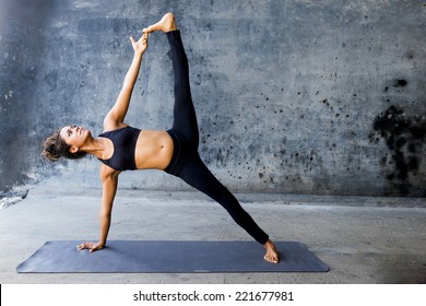 Woman practicing advanced yoga against a dark urban wall - Shutterstock ID 221677981