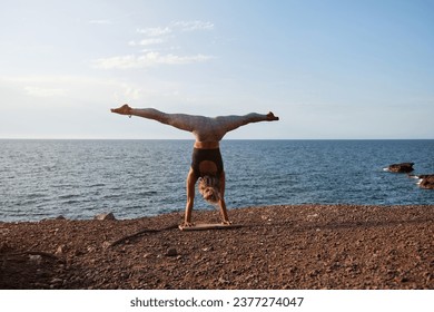 Woman practicing the handstand yoga position with the legs open in front of the sea