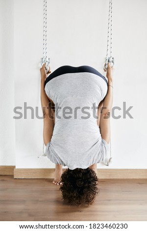 Woman practicing iyengar yoga using wall ropes in studio, supta padangusthasana