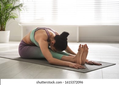 Woman practicing seated forward bend asana in yoga studio. Paschimottanasana pose - Powered by Shutterstock