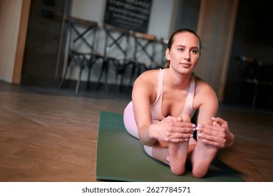 woman practicing seated forward bend on yoga mat in fitness studio. focused on stretching and flexibility training, wearing comfortable sportswear. promotes relaxation and mindful exercise