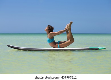 Woman practicing SUP yoga, on a paddleboard in the Caribbean