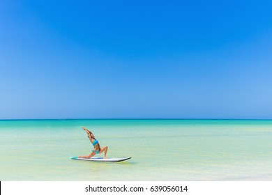 Woman practicing SUP yoga, on a paddle board in the Caribbean