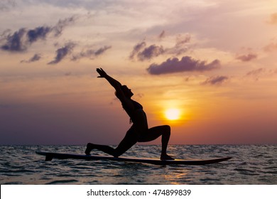 Woman practicing SUP yoga at sunset