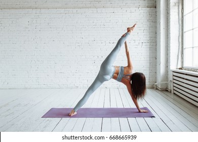 Woman practicing yoga against a white brick (side plank pose, vasisthasana) - Powered by Shutterstock