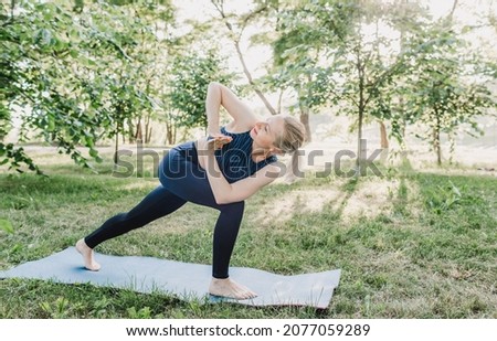 A woman practicing yoga asanas outdoors. A young attractive slender fitness girl in a bodysuit