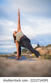 Woman Practicing Yoga In A Beach Setting In The Triangle Position.