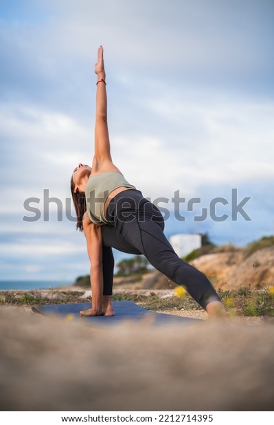 Woman practicing yoga in a beach setting in the\
triangle position.