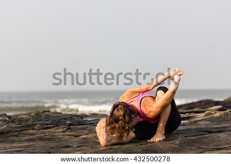 Woman practicing yoga early morning on the rocks by the sea in Goa beach, India. Female yogi on marichyasana pose