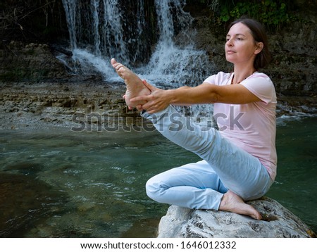 woman is practicing yoga in lotus pose at mountain warefall lake