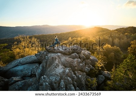 Woman practicing yoga and meditation on the top of huge boulder in the evening. Beautiful sunset, autumn forests, rocks and hills on background. Aerial drone view