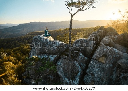 Woman practicing yoga and meditation on the top of huge boulder in the evening. Beautiful sunset, autumn forests, rocks and hills on background. Aerial drone view