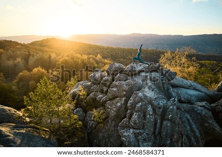 Woman practicing yoga and meditation on the top of huge boulder in the evening. Beautiful sunset, autumn forests, rocks and hills on background. Aerial drone view