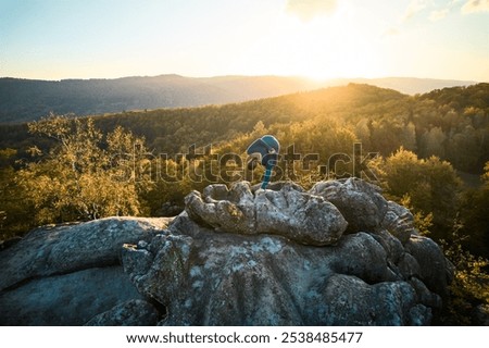 Woman practicing yoga and meditation on the top of huge boulder in the evening. Beautiful sunset, autumn forests, rocks and hills on background. Aerial drone view