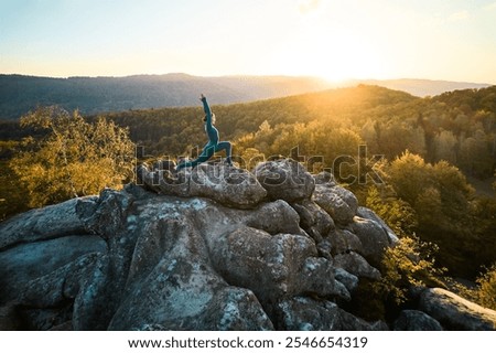 Woman practicing yoga and meditation on the top of huge boulder in the evening. Beautiful sunset, autumn forests, rocks and hills on background. Aerial drone view