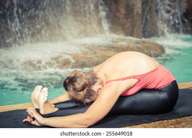 Woman Practicing Yoga Near Waterfall. Seated Forward Fold. Paschimottanasana