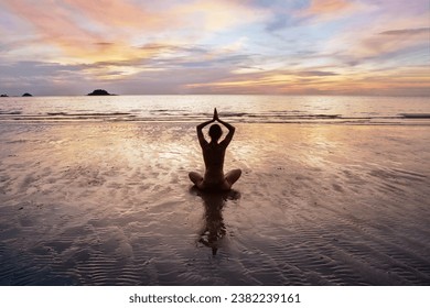 woman practicing yoga on beautiful sunset beach, silhouette of woman meditating, sitting in lotus position