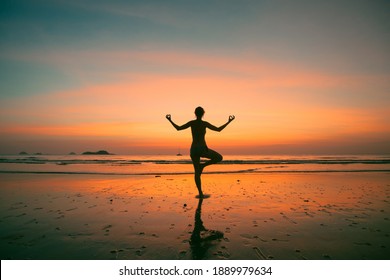 An Woman Practicing Yoga On The Ocean Side, The Silhouette Of Awesome Sunset.