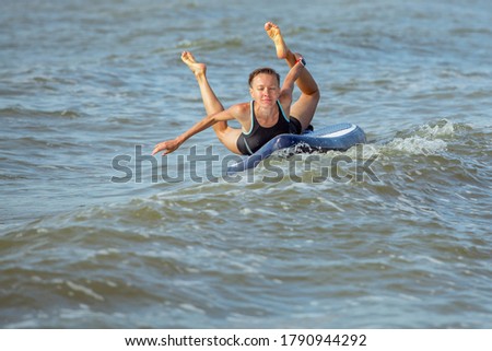 Woman practicing yoga on the paddle board in the morning on a wavy sea