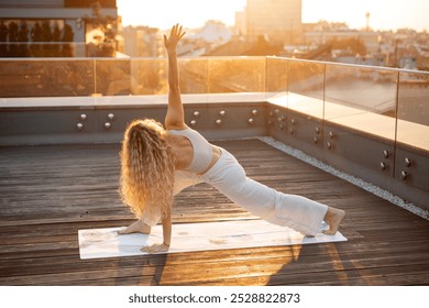 A woman practicing yoga on a rooftop at sunset, performing a side angle pose. - Powered by Shutterstock