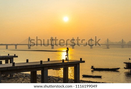 Woman practicing yoga with pier in the river at sunset with bridge in the distance