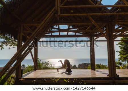 Woman practising a headstand with sunset background. Yoga retreat with bamboo hut and red, orange sky. Handstand balance. Shot in Montanita beach, Ecuador.