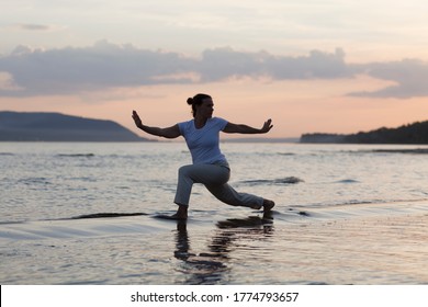 Woman praticing tai chi chuan at sunset on the beach. Chinese management skill Qi's energy. solo outdoor activities. Social Distancing 
