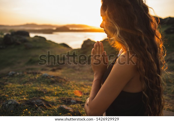 Woman praying\
alone at sunrise. Nature background. Spiritual and emotional\
concept. Sensitivity to\
nature